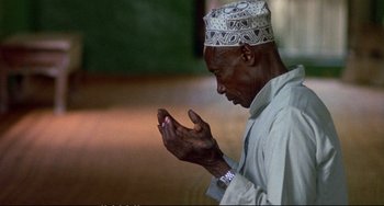 Movie still from “Powaqqatsi” (1988), directed by Godfrey Reggio – An older man is praying with his hands in his hands; Close Up shot, High angle