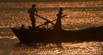 Movie still from “Powaqqatsi” (1988), directed by Godfrey Reggio – Two people in a boat in the water at sunset; Extreme Wide shot, Low angle