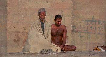 Movie still from “Powaqqatsi” (1988), directed by Godfrey Reggio – A man sitting next to another man on the ground; Wide shot, High angle