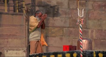 Movie still from “Powaqqatsi” (1988), directed by Godfrey Reggio – An old man is praying in front of a pillar; Wide shot, High angle