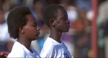 Movie still from “Powaqqatsi” (1988), directed by Godfrey Reggio – Two young men standing next to each other in front of a crowd of onlookers; Close Up shot, Low angle