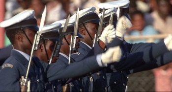 Movie still from “Powaqqatsi” (1988), directed by Godfrey Reggio – A group of men in uniform holding up knives; Medium shot, High angle