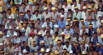 Movie still from “Powaqqatsi” (1988), directed by Godfrey Reggio – A large group of men wearing hats and sitting in a stadium; Extreme Wide shot, High angle