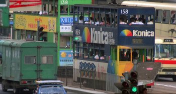 Movie still from “Powaqqatsi” (1988), directed by Godfrey Reggio – A double decker bus driving down a street past buildings; Extreme Wide shot, High angle