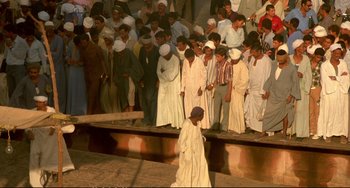 Movie still from “Powaqqatsi” (1988), directed by Godfrey Reggio – A group of people standing in front of a crowd; Extreme Wide shot, High angle
