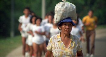 Movie still from “Powaqqatsi” (1988), directed by Godfrey Reggio – An older woman carrying a bag on top of her head; Medium shot, High angle