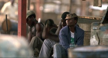 Movie still from “Powaqqatsi” (1988), directed by Godfrey Reggio – A group of men sitting next to each other on the ground; Medium shot, Low angle