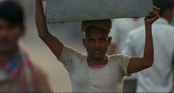 Movie still from “Powaqqatsi” (1988), directed by Godfrey Reggio – A man holding a piece of concrete over his head; Medium shot, Low angle