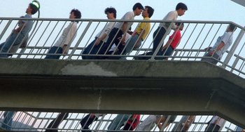 Movie still from “Powaqqatsi” (1988), directed by Godfrey Reggio – A group of young men walking across a bridge; Wide shot, Overhead angle