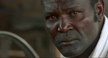 Movie still from “Powaqqatsi” (1988), directed by Godfrey Reggio – A man's face with yellow eyes; Close Up shot, Over the shoulder angle