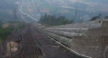 Movie still from “Powaqqatsi” (1988), directed by Godfrey Reggio – A view of a train track with a train on it's side; Extreme Wide shot, High angle