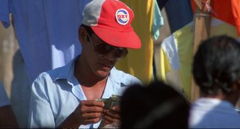 Movie still from “Powaqqatsi” (1988), directed by Godfrey Reggio – A man in a red hat is looking at his cell phone; Close Up shot, Over the shoulder angle