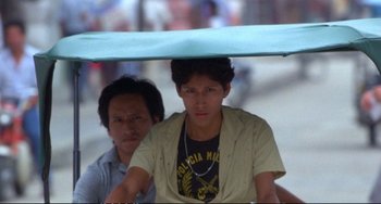Movie still from “Powaqqatsi” (1988), directed by Godfrey Reggio – A man riding a bike with a man holding an umbrella over his head; Medium shot, Low angle
