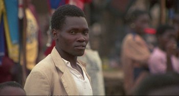 Movie still from “Powaqqatsi” (1988), directed by Godfrey Reggio – A man in a beige jacket is looking at the camera; Close Up shot, Over the shoulder angle