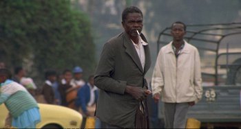 Movie still from “Powaqqatsi” (1988), directed by Godfrey Reggio – An older man smoking a cigarette while walking down the street; Wide shot, Low angle
