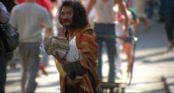 Movie still from “Powaqqatsi” (1988), directed by Godfrey Reggio – A man with long hair is holding newspapers; Wide shot, High angle