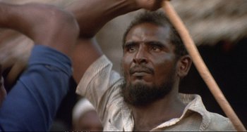 Movie still from “Powaqqatsi” (1988), directed by Godfrey Reggio – A person holding a baseball bat; Close Up shot, Over the shoulder angle