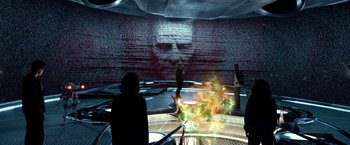 Movie still from “Power Rangers” (2017), directed by Dean Israelite – A group of people standing in front of a wall with an image of a man's face projected on it; Wide shot, Over the shoulder angle