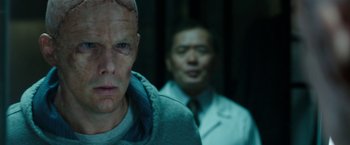 Movie still from “Predestination” (2014), directed by Michael Spierig – A man with a shaved head is standing next to another man in a suit; Close Up shot, Over the shoulder angle