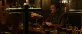 Movie still from “Predestination” (2014), directed by Michael Spierig – A woman sitting at a table with a glass of beer; Medium shot, Over the shoulder angle