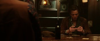 Movie still from “Predestination” (2014), directed by Michael Spierig – A man sitting at a table with a bottle of wine; Medium shot, Over the shoulder angle