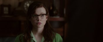Movie still from “Predestination” (2014), directed by Michael Spierig – A young woman wearing glasses and a green shirt looking at the camera; Close Up shot, Over the shoulder angle