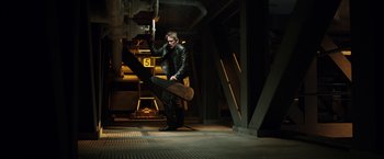 Movie still from “Predestination” (2014), directed by Michael Spierig – A man holding a skate board in a dark room; Wide shot, Low angle