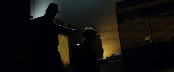 Movie still from “Predestination” (2014), directed by Michael Spierig – A man is standing in the dark while another man holds a cell phone; Medium shot, Over the shoulder angle