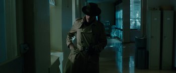 Movie still from “Predestination” (2014), directed by Michael Spierig – A man in a trench coat and a hat is holding a camera; Medium shot, Low angle
