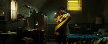 Movie still from “Predestination” (2014), directed by Michael Spierig – A man holding a guitar case in a dark room; Medium shot, Low angle