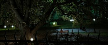 Movie still from “Predestination” (2014), directed by Michael Spierig – A person sitting on top of a park bench under a tree; Extreme Wide shot, High angle