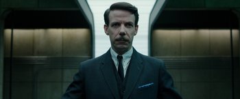 Movie still from “Predestination” (2014), directed by Michael Spierig – A man in a suit and tie standing in front of a building; Close Up shot, Low angle