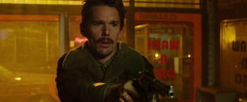 Movie still from “Predestination” (2014), directed by Michael Spierig – A man holding a gun while standing in front of a building; Close Up shot, Over the shoulder angle