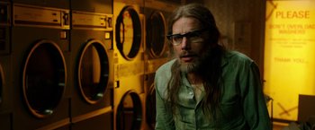 Movie still from “Predestination” (2014), directed by Michael Spierig – A man with long hair and glasses in front of a washing machine; Close Up shot, Over the shoulder angle