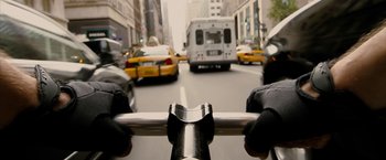 Movie still from “Premium Rush” (2012), directed by David Koepp – A view from a bicycle handlebar of a city street with cars driving on it; Extreme Close Up shot, Low angle