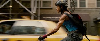 Movie still from “Premium Rush” (2012), directed by David Koepp – A woman riding a bike down a street past a taxi cab; Medium shot, Low angle