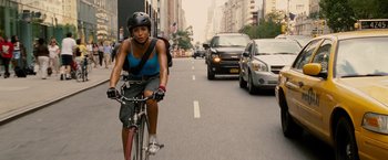 Movie still from “Premium Rush” (2012), directed by David Koepp – A woman riding a bike down a street with cars behind it; Medium shot, Over the shoulder angle