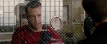 Movie still from “Premium Rush” (2012), directed by David Koepp – A man in a red shirt is behind a fence; Close Up shot, Over the shoulder angle