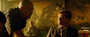 Movie still from “Premium Rush” (2012), directed by David Koepp – A group of men sitting around a table talking to each other; Medium shot, Over the shoulder angle