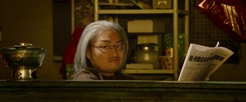 Movie still from “Premium Rush” (2012), directed by David Koepp – A man with long gray hair sitting in front of a computer; Close Up shot, Low angle