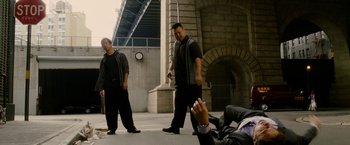 Movie still from “Premium Rush” (2012), directed by David Koepp – A group of men standing next to each other on a sidewalk; Wide shot, Over the shoulder angle
