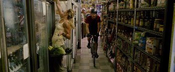 Movie still from “Premium Rush” (2012), directed by David Koepp – A man riding a bike down the middle of a grocery store; Wide shot, Over the shoulder angle