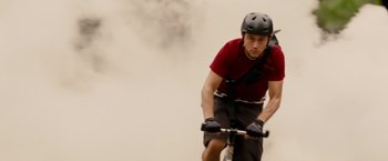 Movie still from “Premium Rush” (2012), directed by David Koepp – A man riding a bike on a cloudy day; Medium shot, Low angle