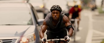 Movie still from “Premium Rush” (2012), directed by David Koepp – A bicyclist wearing a helmet; Medium shot, Low angle