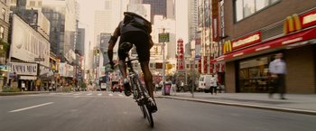Movie still from “Premium Rush” (2012), directed by David Koepp – A man riding a bike down the street in the city; Wide shot, Low angle