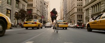 Movie still from “Premium Rush” (2012), directed by David Koepp – A man riding a bike down the middle of a street; Wide shot, Low angle