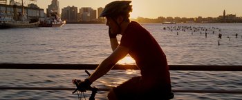 Movie still from “Premium Rush” (2012), directed by David Koepp – A man riding a bike on top of a body of water; Medium shot, Over the shoulder angle