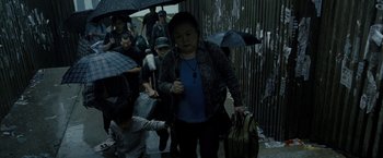 Movie still from “Premium Rush” (2012), directed by David Koepp – A group of people walking down a street under umbrellas; Medium shot, High angle