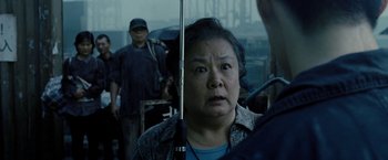 Movie still from “Premium Rush” (2012), directed by David Koepp – An older asian woman holding onto an umbrella in the rain; Close Up shot, Over the shoulder angle