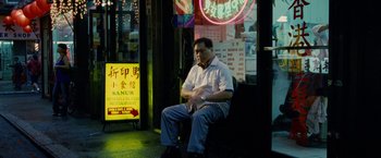 Movie still from “Premium Rush” (2012), directed by David Koepp – A man sitting on a bench in front of a store; Wide shot, High angle